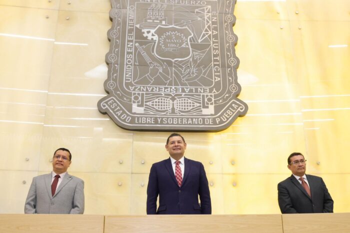 Gobernador Alejandro Armenta en el centro del recinto legislativo de Puebla, con el escudo estatal al fondo.
