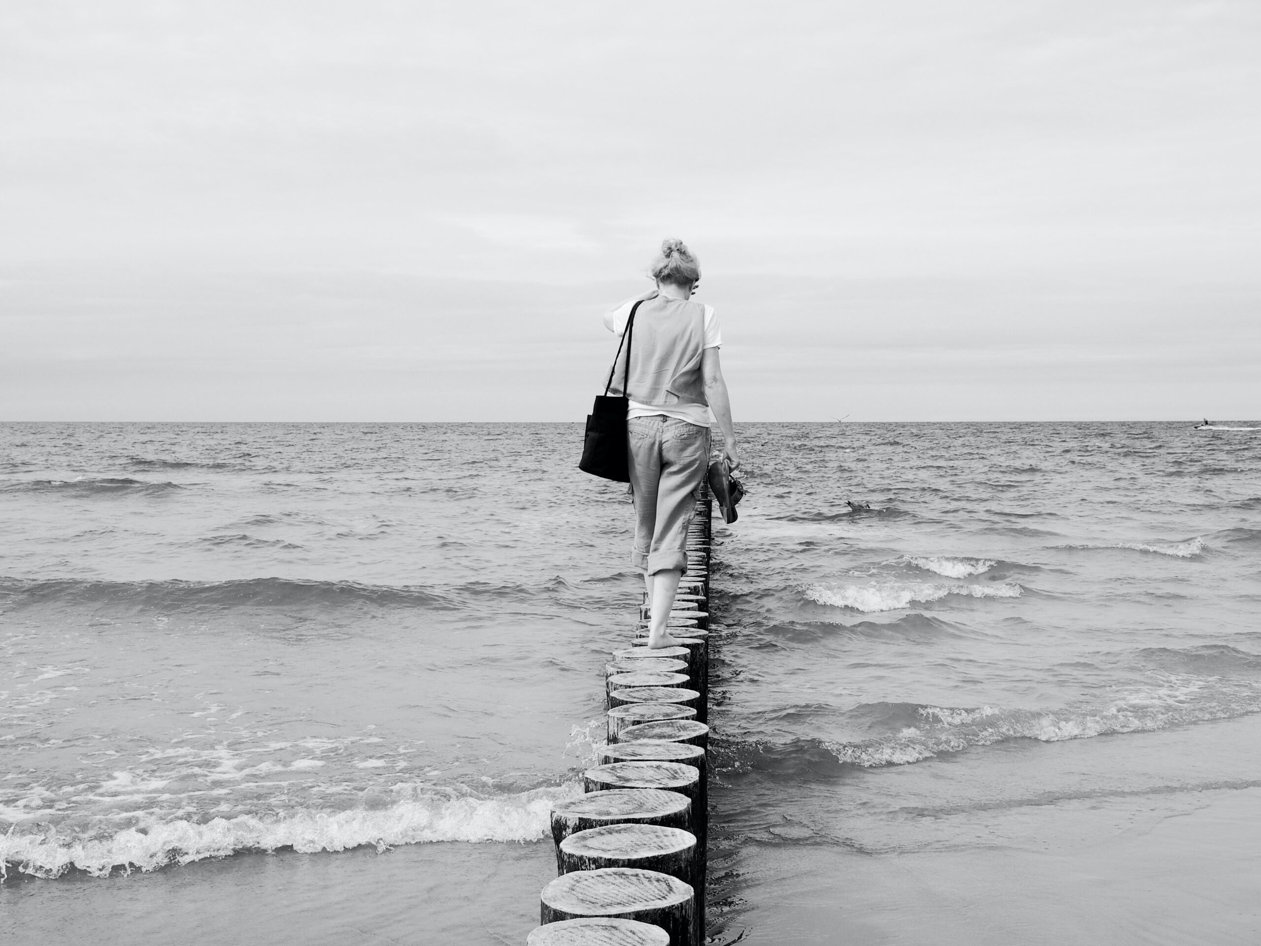 abuelita en el mar | Ruiz Healy Times Person walking away along a circular wooden jetty that extends into the ocean, carrying a bag on their shoulder.