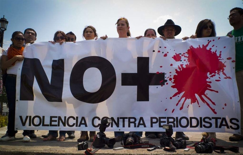 Group of people holding a banner that reads 'NO+ Violencia Contra Periodistas' with red paint splatters, protesting for journalist safety.