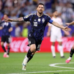 Argentine footballer wearing the number 10 jersey celebrates with arms outstretched on a soccer field.