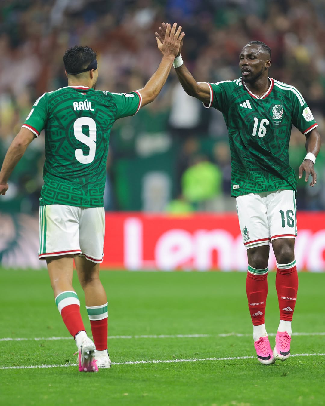 Two Mexican soccer players in green uniforms high-five on a green field after a play, Raul #9 on left and #16 on right.