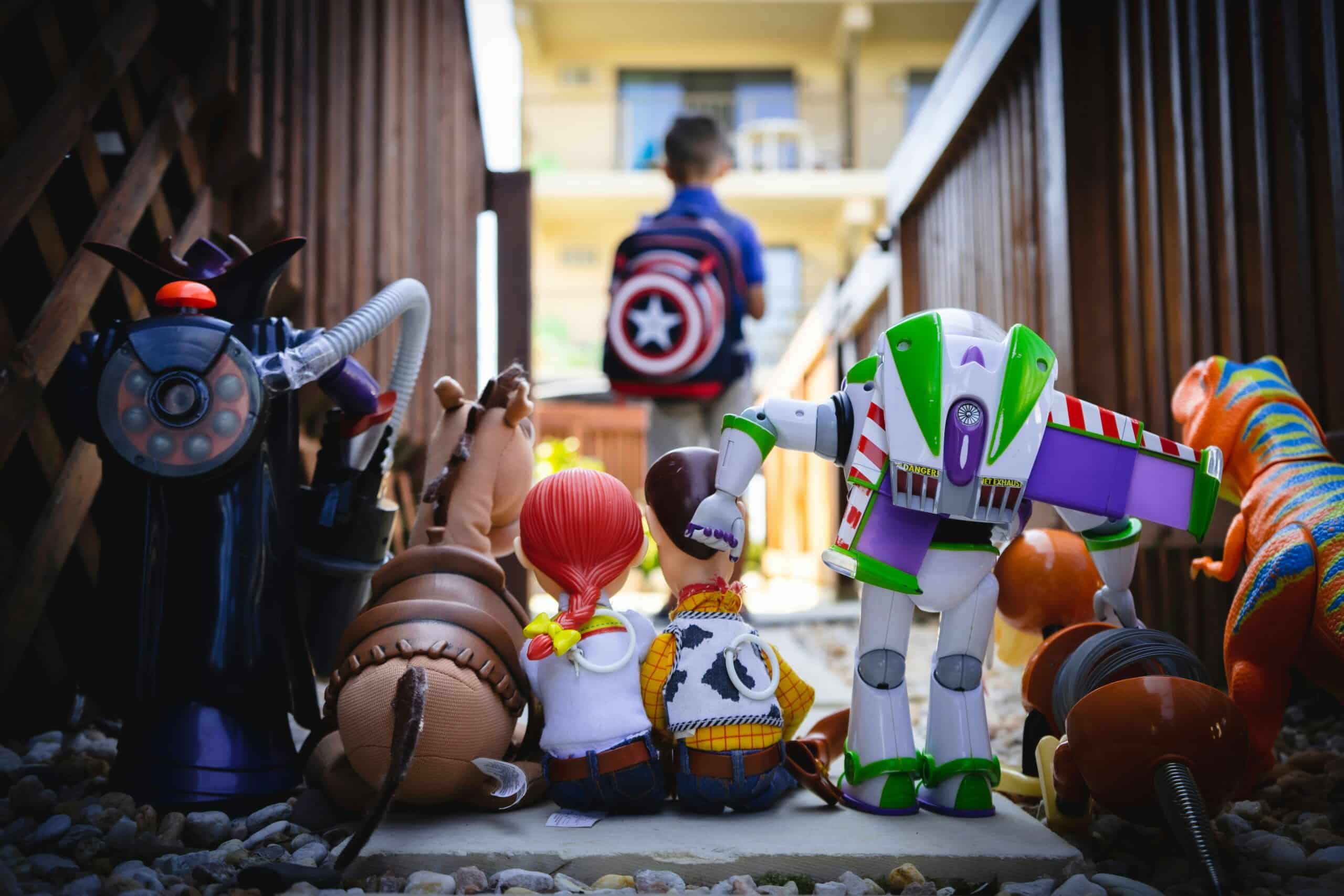 Row of colorful toys and action figures lined up, with a child wearing a Captain America backpack in the background.