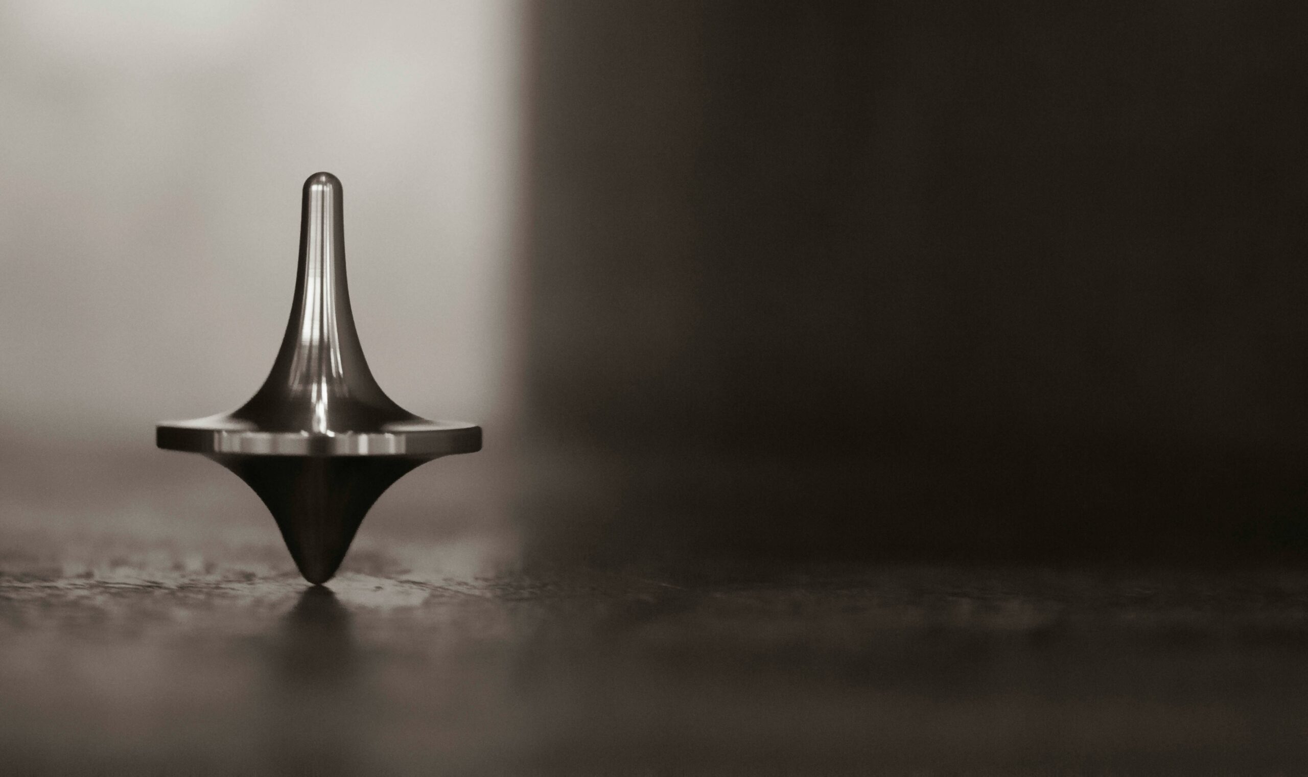 Close-up of a metallic spinning top standing on its tip on a wooden surface.
