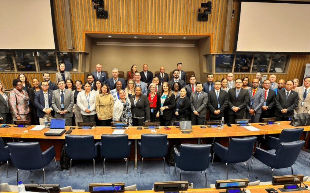 Large group of professionals in suits and dresses posing for a group photo in a formal conference room with a long wood table and blue chairs.