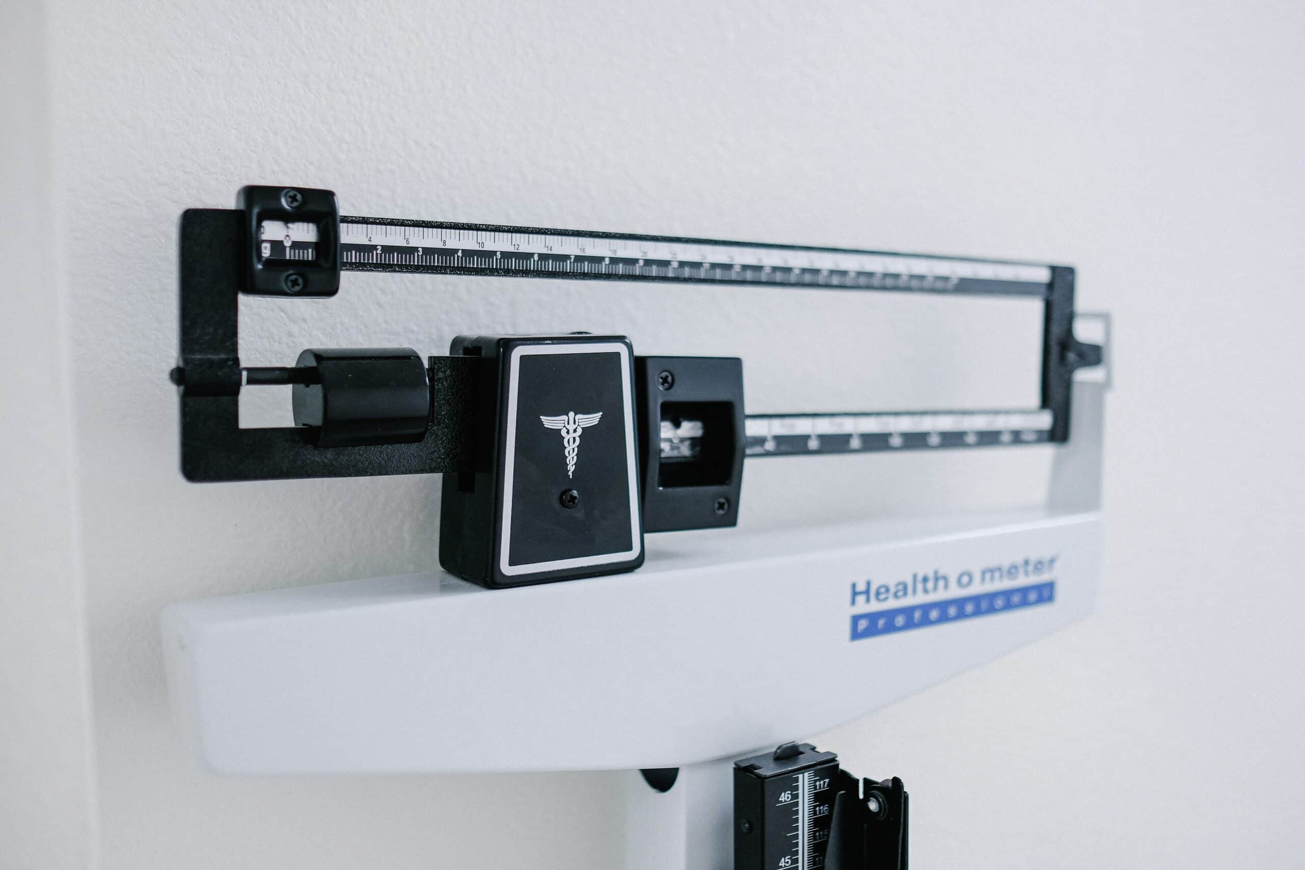Clinical health scale with a long measurement beam, sliding weight, and Healthometer branding in a clinic setting.