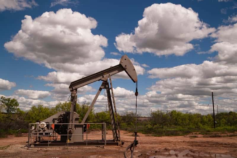 Oil pumpjack operating in a desert-like field under a bright, partly cloudy sky