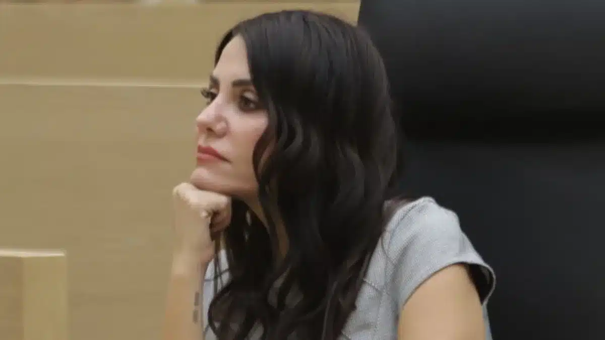 Side profile of a woman with long dark hair resting her chin on her hand, looking thoughtful in a neutral setting.